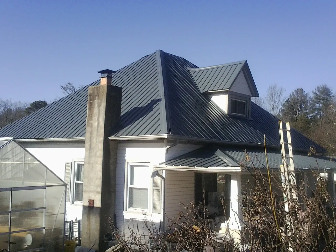 Dark blue standing seam metal roof on a white farmhouse with dormer — Slate & Tile Roof Repair by Roofing Brothers in Munnsville