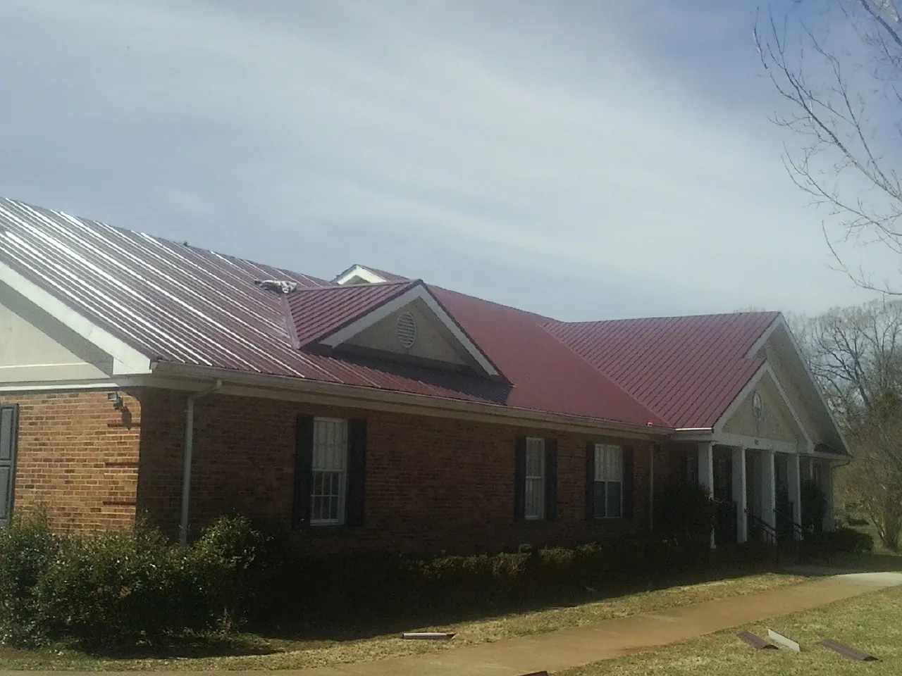 Red metal roof with gabled entries on a long brick building, from a Hail Damage Roof Repair job in Munnsville