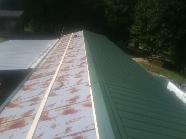 Old rusted panels beside newly installed green metal roofing — Wind Damage Roof Repair by Roofing Brothers in Munnsville
