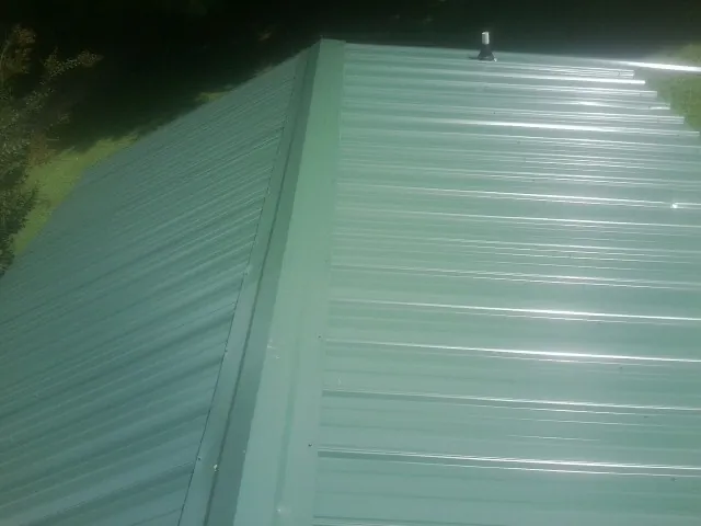 New green metal panels meeting at the ridge of a roof — Flat Roof Repair work by our crew in Munnsville