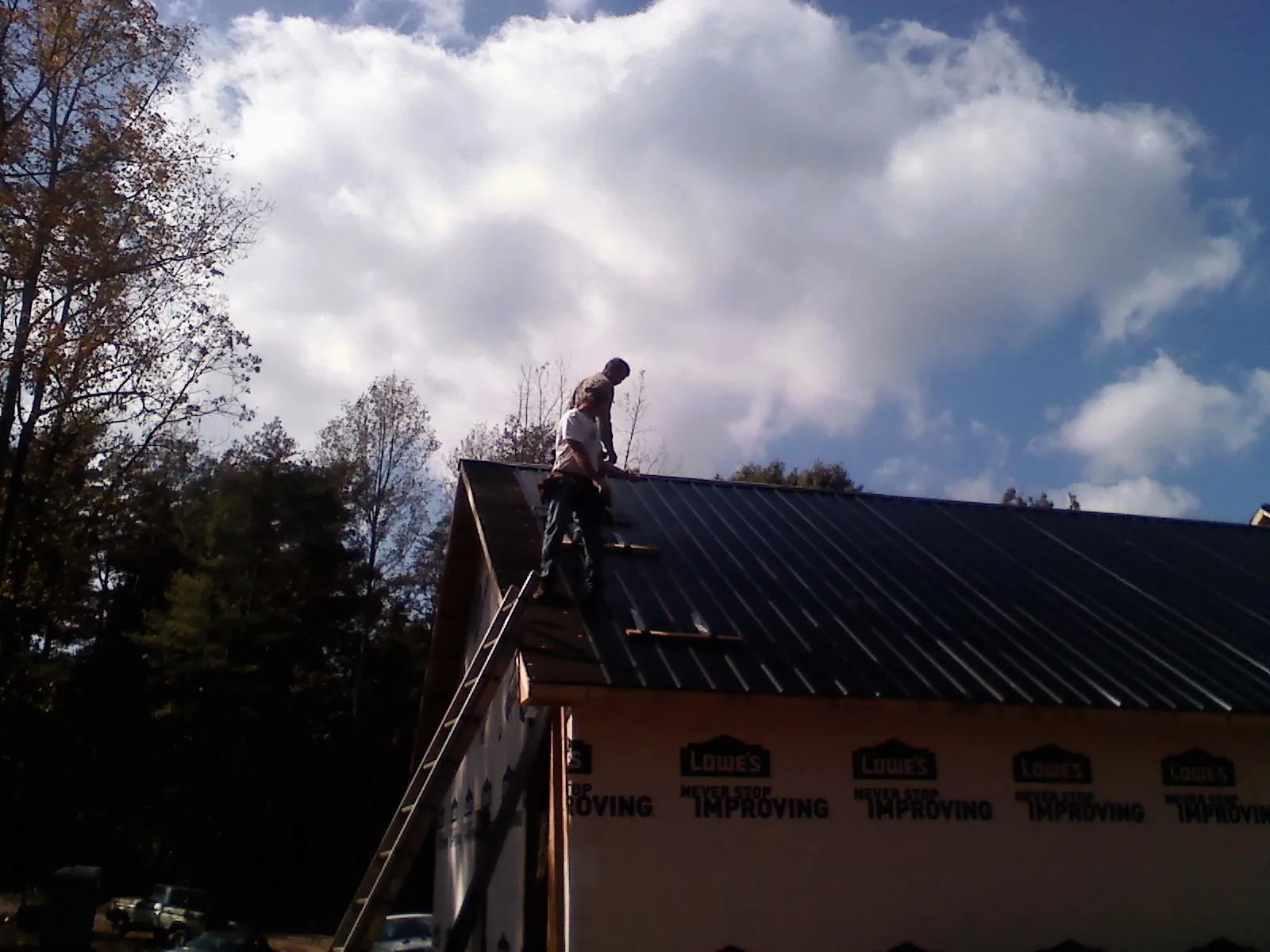 Roofer fastening dark metal panels high against a cloudy sky, from a Roof Inspection job in Munnsville