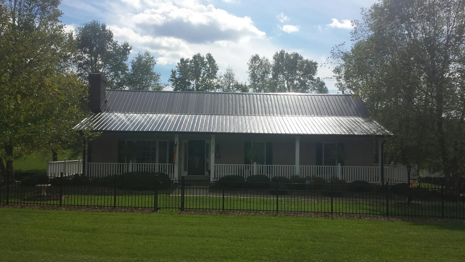 Gray metal roof on a brick ranch with a full width front porch — Gutter Guard Installation work by our crew in Munnsville