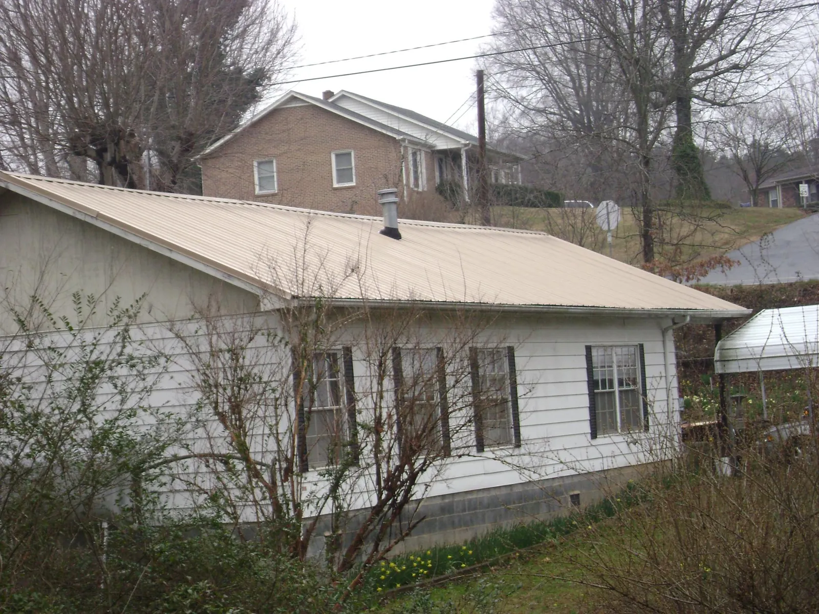 Tan metal roof on a white sided house set into a hillside — Commercial Roofing by Roofing Brothers in Munnsville