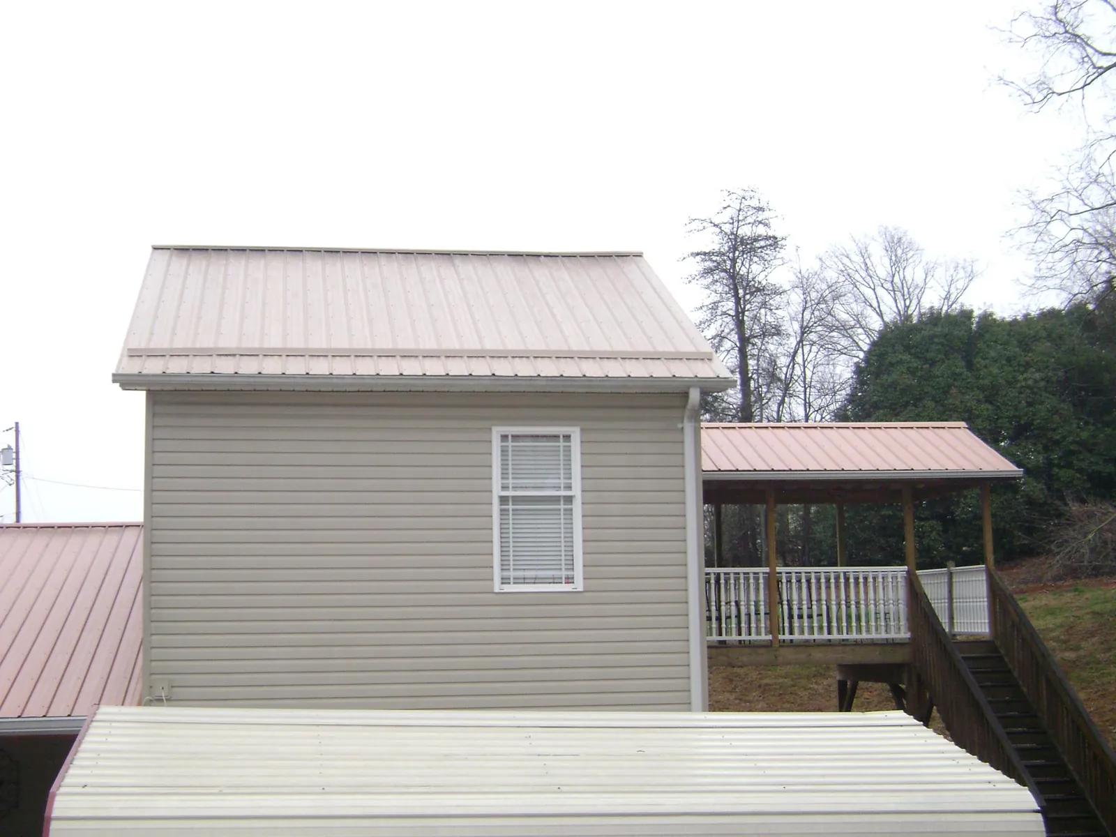 Tan metal roofs on a two story addition and attached porch, from a Roof Replacement job in Munnsville